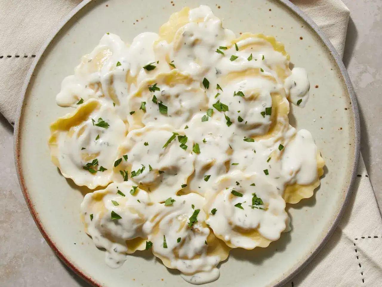 Ravioli w kremowym sosie śmietanowym, posypane natką pietruszki, na talerzu.