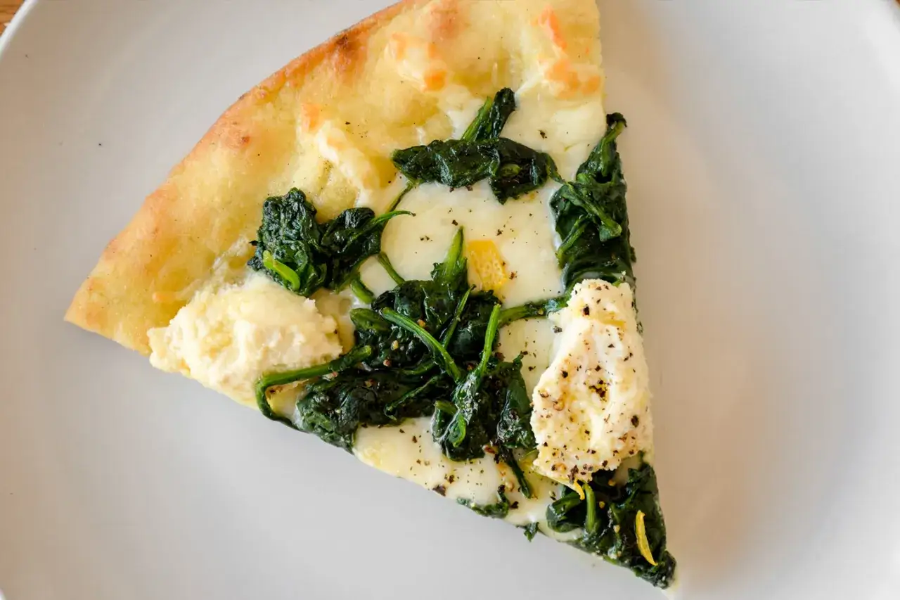 Kawałek pysznej pizzy ze szpinakiem i serem, z chrupiącym ciastem i aromatycznymi dodatkami.