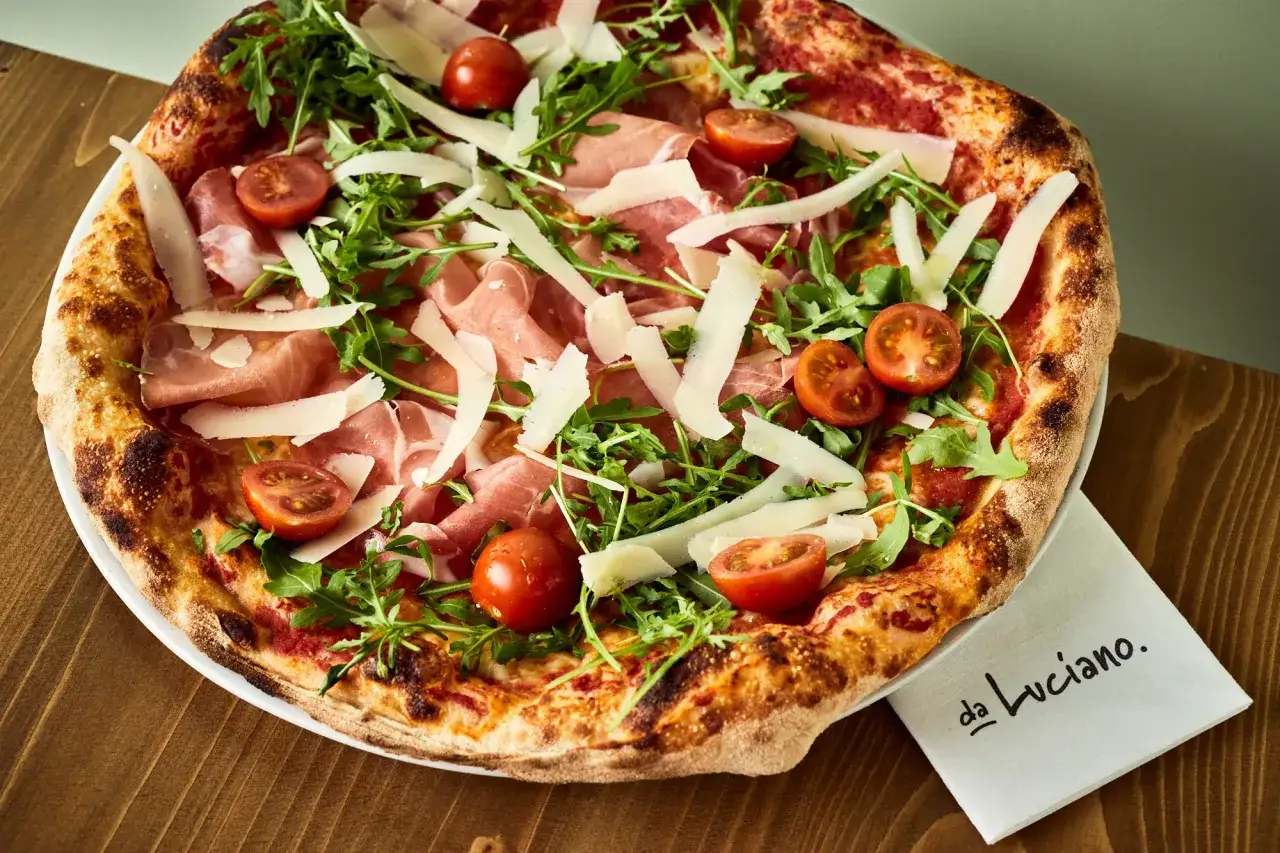 Pizza z rukolą, pomidorkami i szynką parmeńską. Niezbędny dodatek smakowy włoskiej pizzy, który zachwyca świeżością i aromatem.