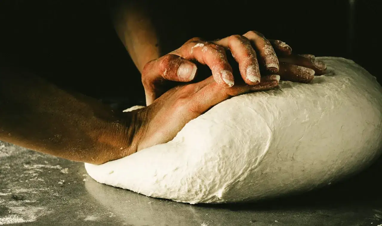 Dłonie ugniatające puszyste ciasto na pizzę neapolitańską. Mąka lekko oprósza palce i blat.