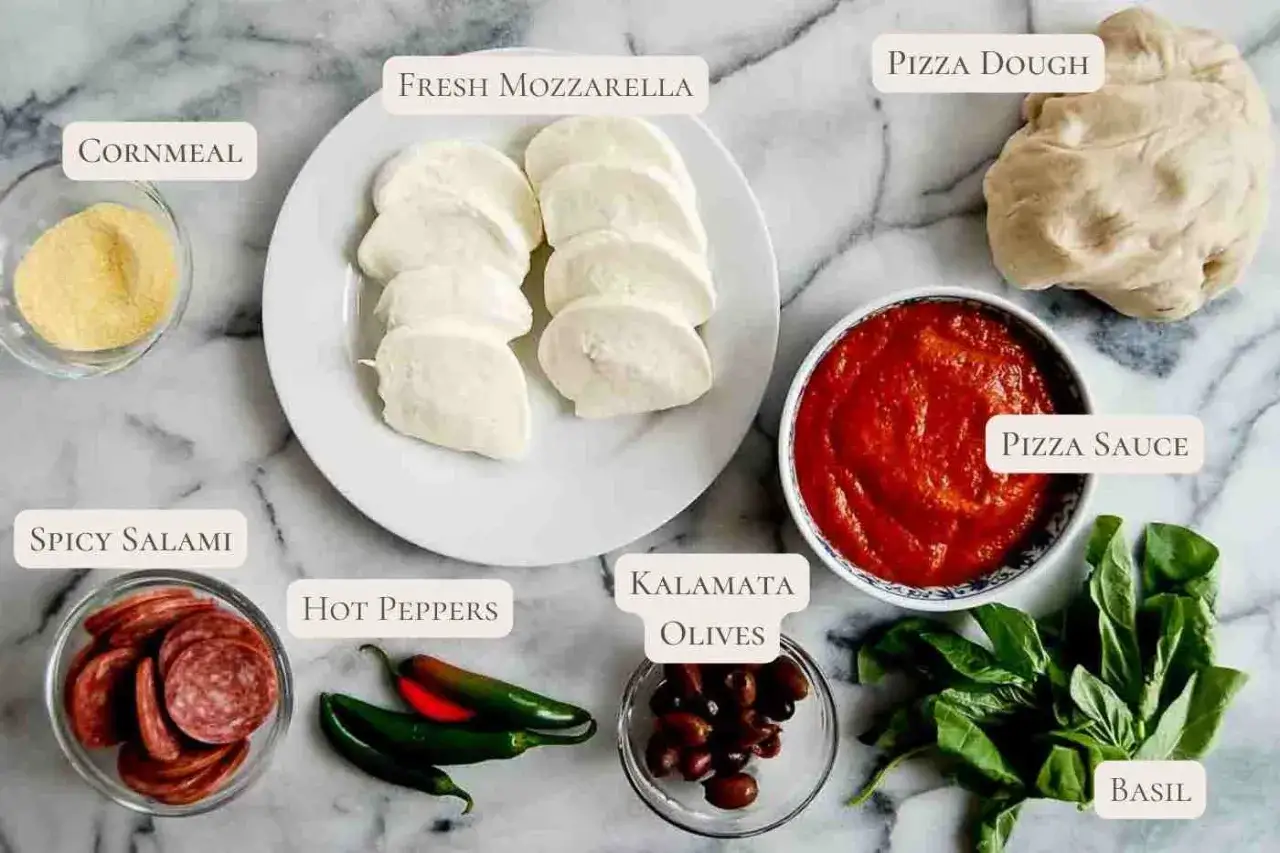 Składniki na pizzę: ciasto, sos, mozzarella, pikantne salami, oliwki, papryczki i bazylia.