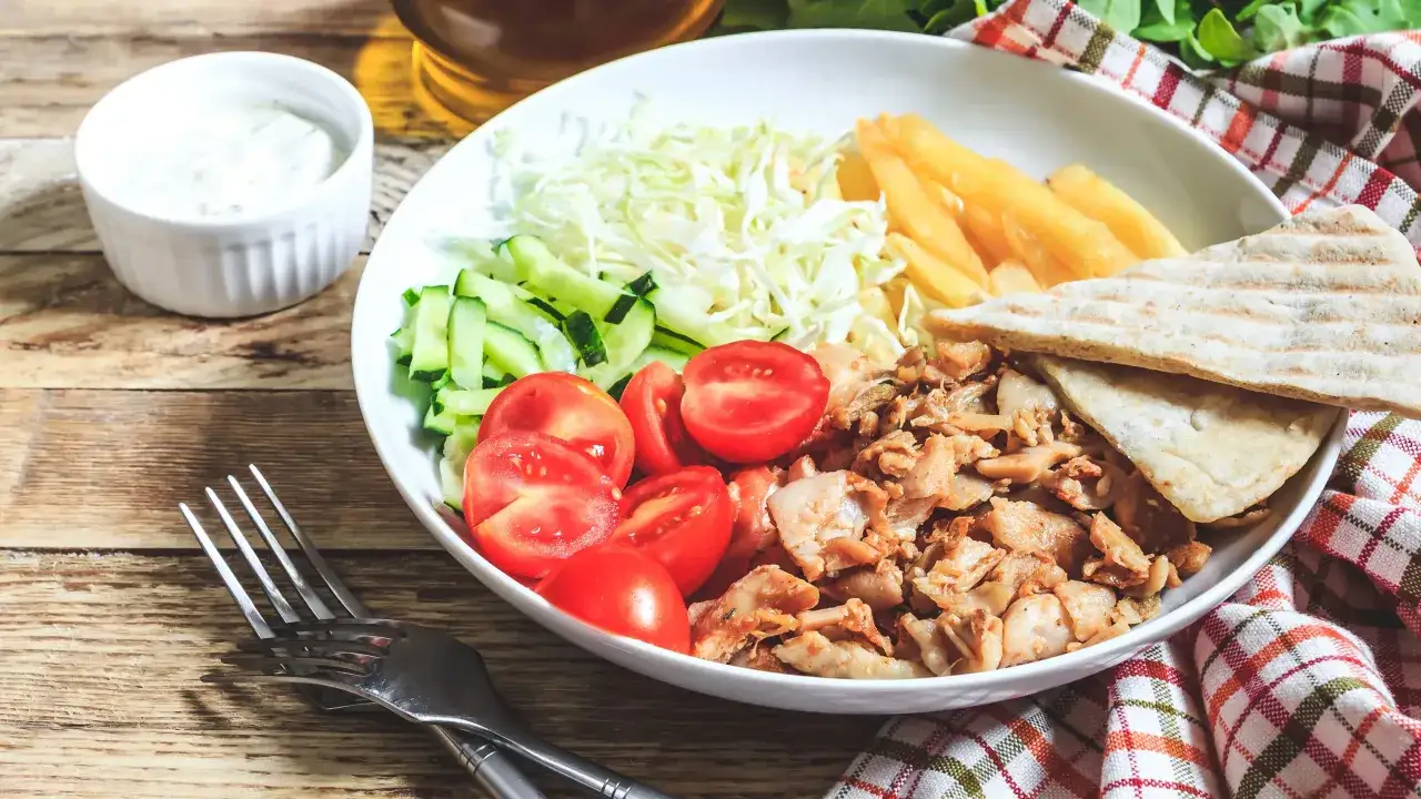 Pyszny gyros z kurczaka z frytkami, warzywami i chlebkiem pita, podany z kremowym sosem do gyrosa.