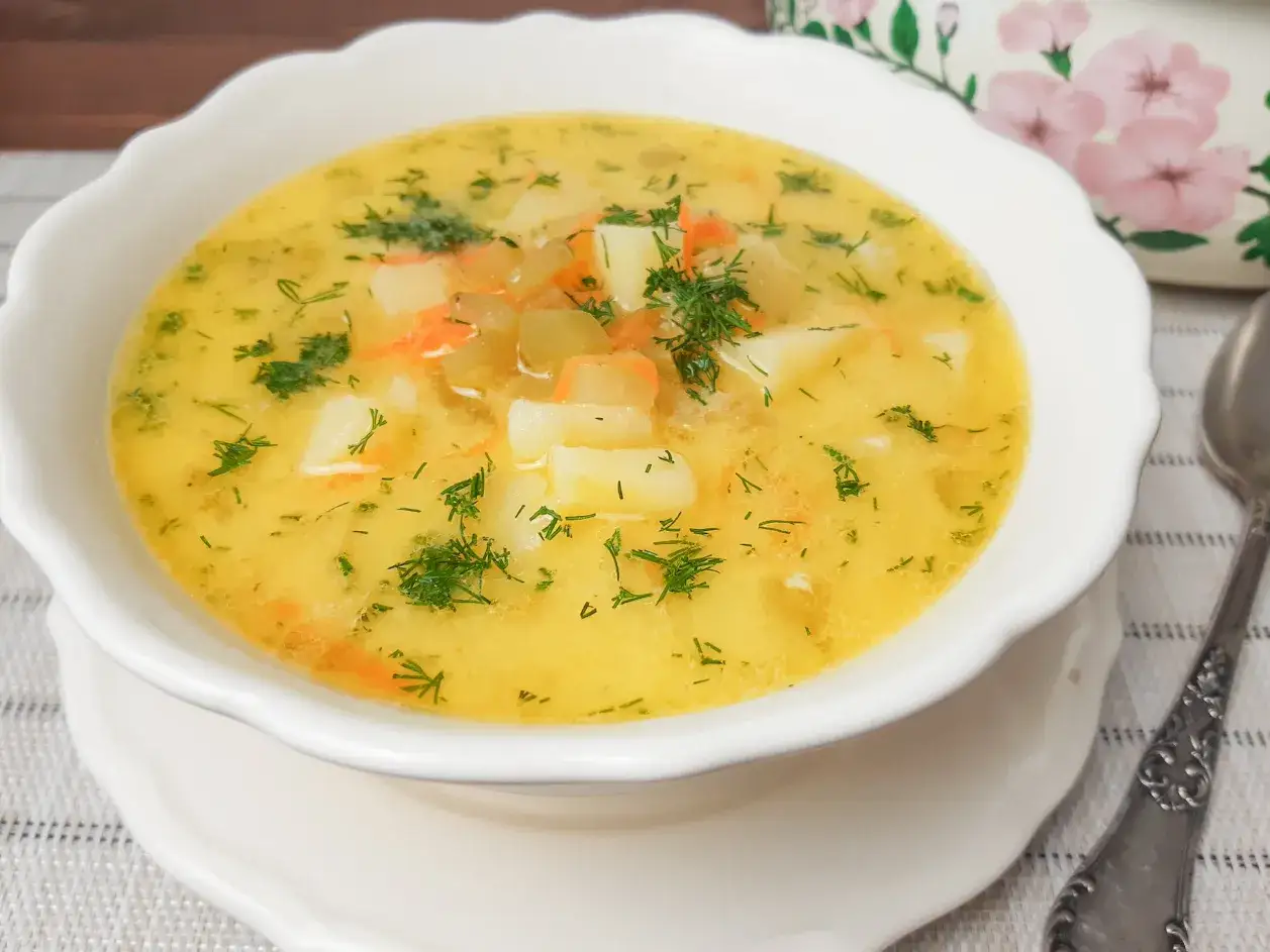 Zupa ogórkowa przepis babci. Aromatyczna, domowa zupa z ziemniakami, marchewką i koperkiem, podana w białej miseczce.