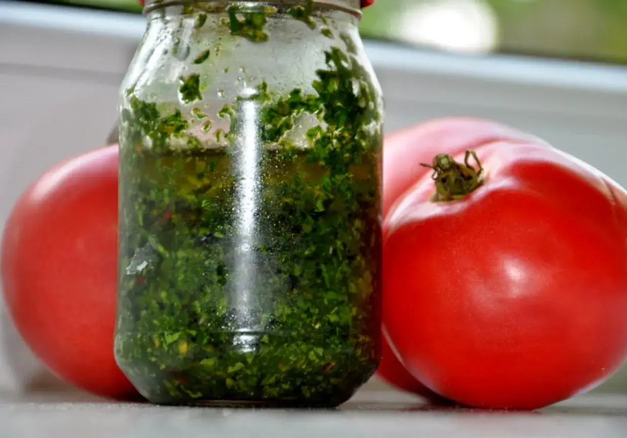 Słoik z domowym pesto z pietruszki, otoczony dojrzałymi pomidorami. Idealny dodatek do letnich dań.
