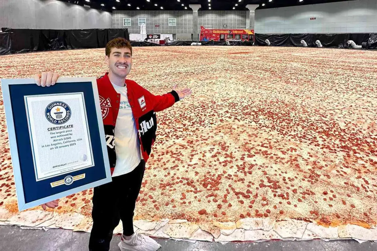 Mężczyzna z certyfikatem Guinnessa prezentuje największą pizzę świata, która rozciąga się na ogromnej przestrzeni.