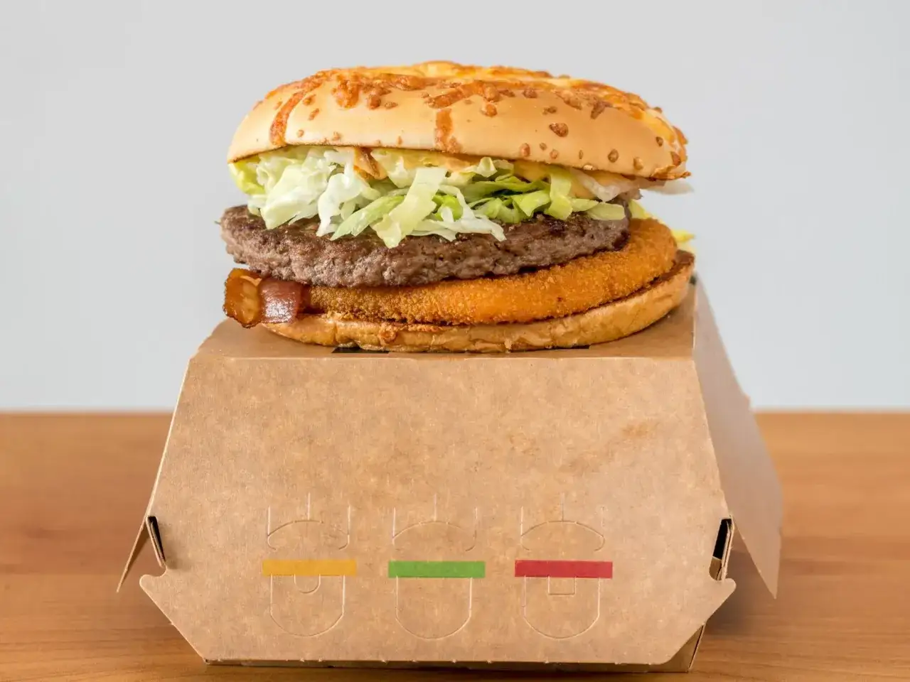 Drwal z chrzanem, czyli soczysty burger z chrupiącym kotletem i warzywami, w papierowym opakowaniu z kolorowymi akcentami.