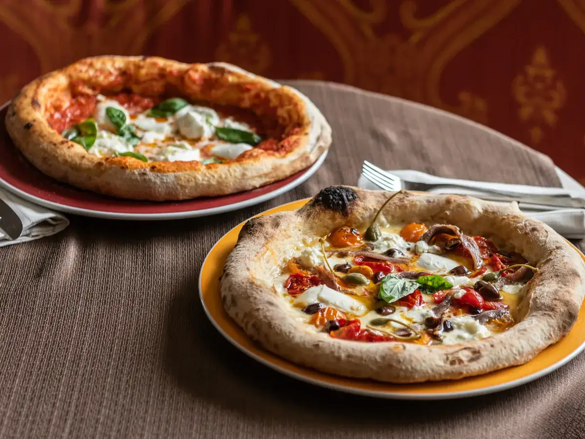 Dwie pyszne pizze neapolitańskie, jedna z burratą i bazylią, druga z anchois i kaparami. Niezbędny dodatek smakowy włoskiej pizzy.