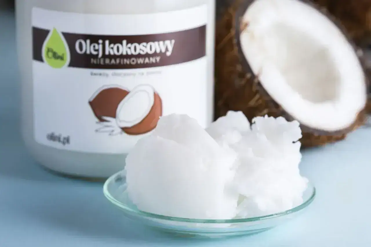 Olej kokosowy nierafinowany na talerzyku, obok połówka kokosa i słoik. Idealny jako olej do smażenia.
