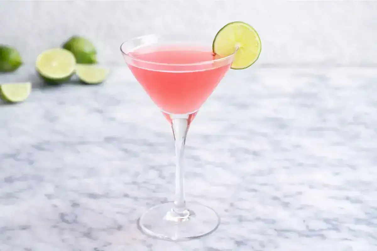 Różowy cosmopolitan w kieliszku, ozdobiony plasterkiem limonki, na marmurowym blacie. Idealny na wieczór w stylu cosmopolitan.