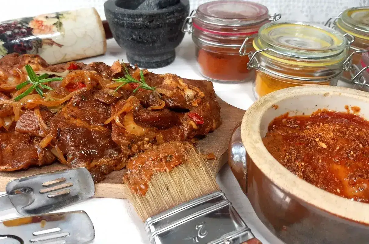 Karkówka na grilla w aromatycznej marynacie, gotowa do pieczenia. Obok pędzel z marynatą i słoiczki z przyprawami.