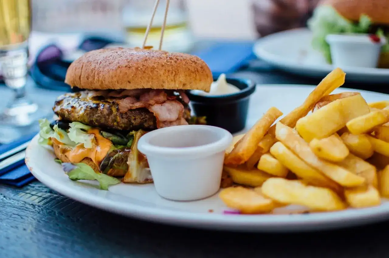 Pyszny burger z bekonem i frytki na talerzu. Idealny sposób, jak jeść burgera w restauracji, by delektować się każdym kęsem.