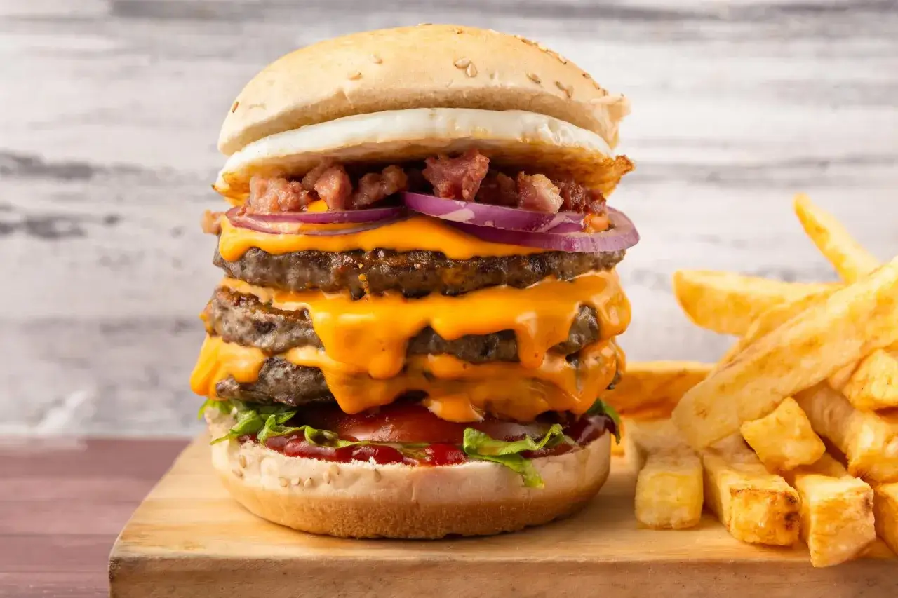 Potrójny cheeseburger z rozpływającym się serem, boczkiem i jajkiem, obok frytki. Idealny przepis, jak zrobic cheeseburgera z mc.