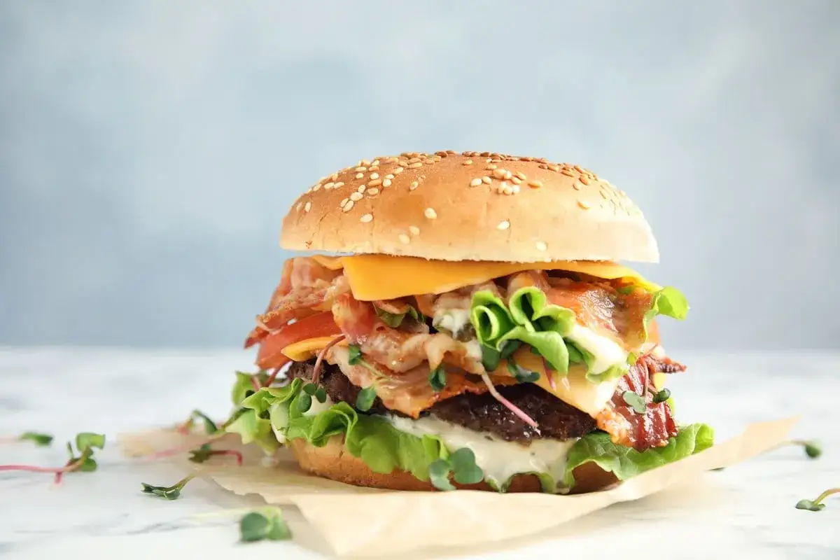Apetyczny burger z bekonem, serem i warzywami. Zastanawiasz się, ile kalorii ma burger w restauracji? Ten wygląda na bogaty w smaku i kalorie.