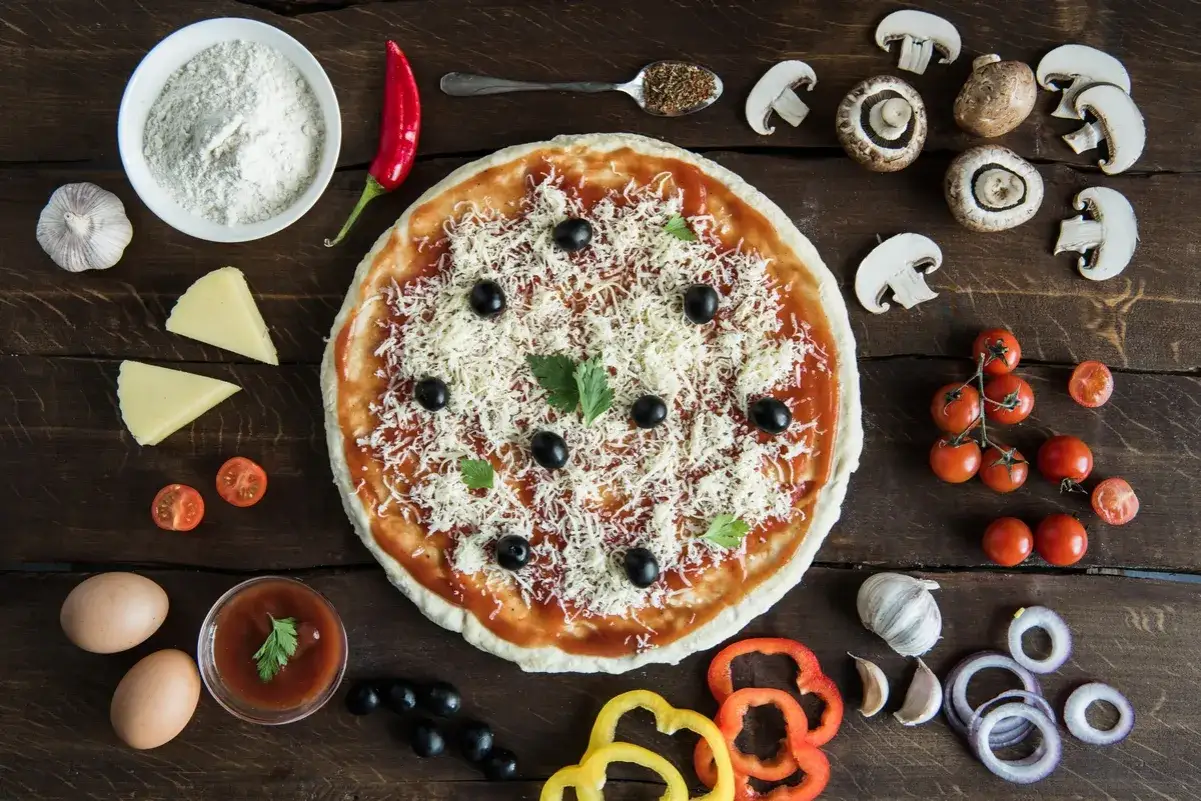 Na pizzy i wokół niej składniki: pieczarki, pomidorki, oliwki, ser, jajka, czosnek, papryka, cebula. Jakie pieczarki do pizzy? Te na zdjęciu wyglądają idealnie!