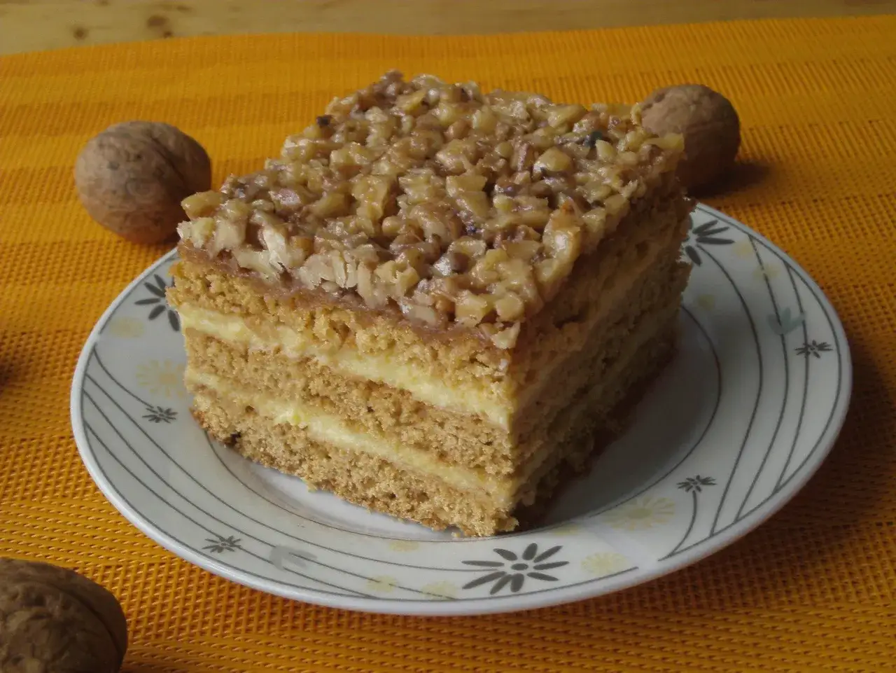 Pyszny, wielowarstwowy tort orzechowy, jeden z 10 najlepszych ciast, na talerzyku z orzechami w tle.