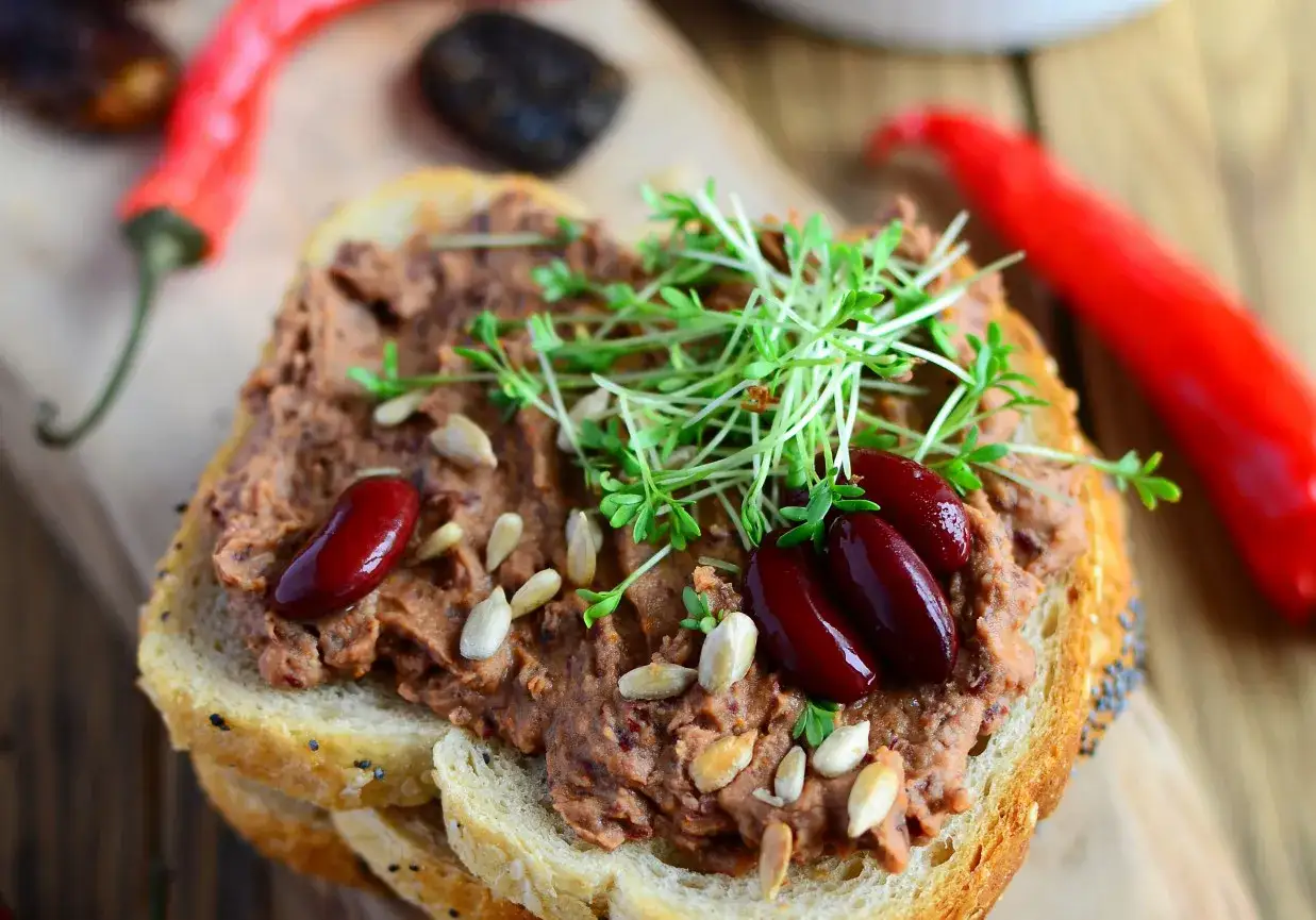 Pyszna pasta z czerwonej fasoli na chlebie, ozdobiona kiełkami i nasionami. Obok czerwone papryczki chili.