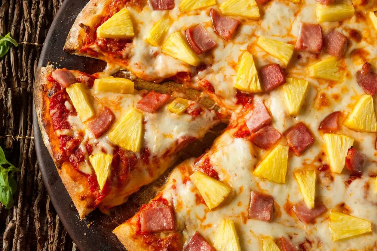 Pizza hawajska, której kto wymyślił, z ananasem i szynką, wygląda apetycznie.
