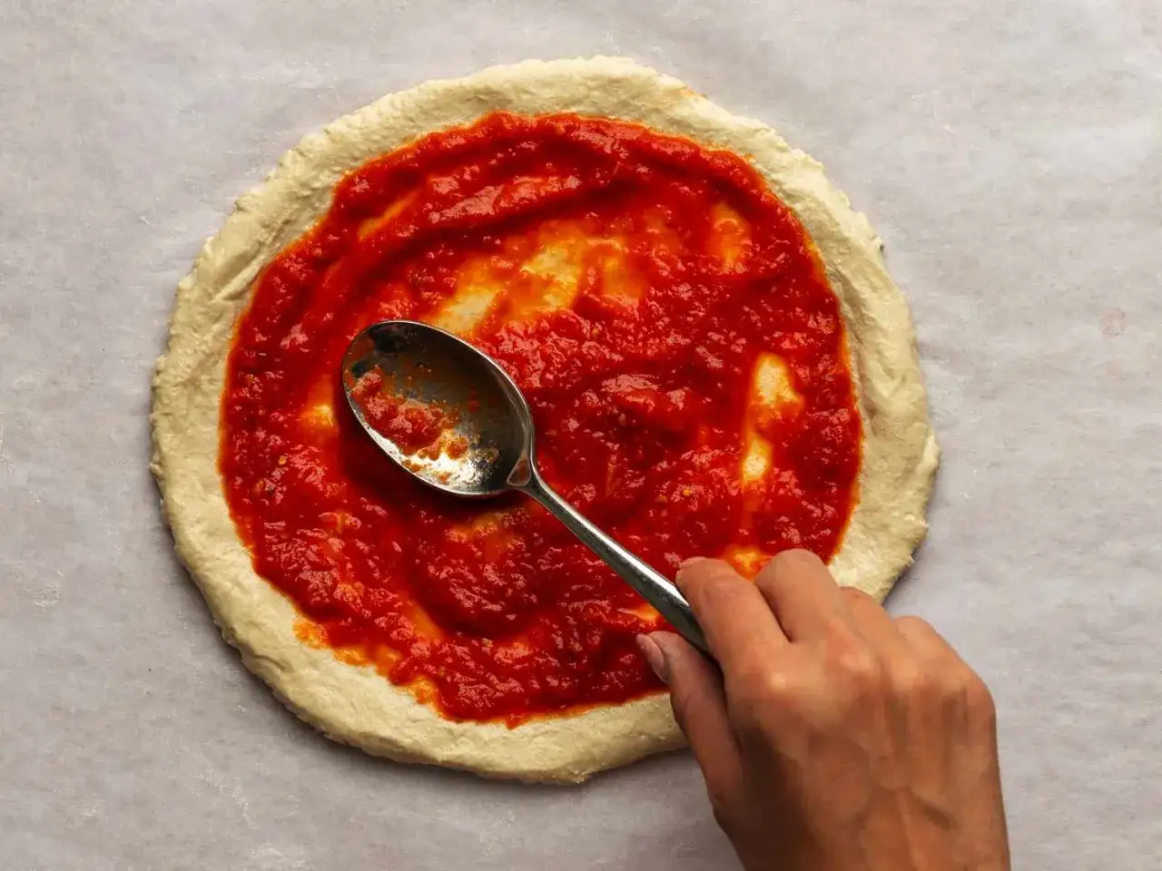 Rozsmarowywanie sosu pomidorowego na cieście pizzy. To kluczowy krok w przygotowaniu idealnego przepisu na pizzę.
