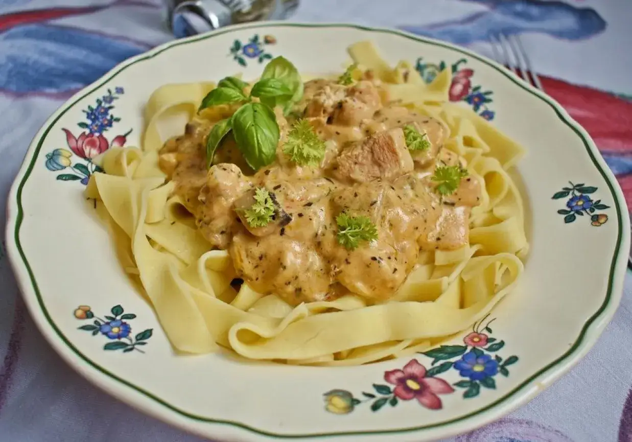 Pyszny kurczak w sosie serowym na tagliatelle, udekorowany bazylią i natką pietruszki.