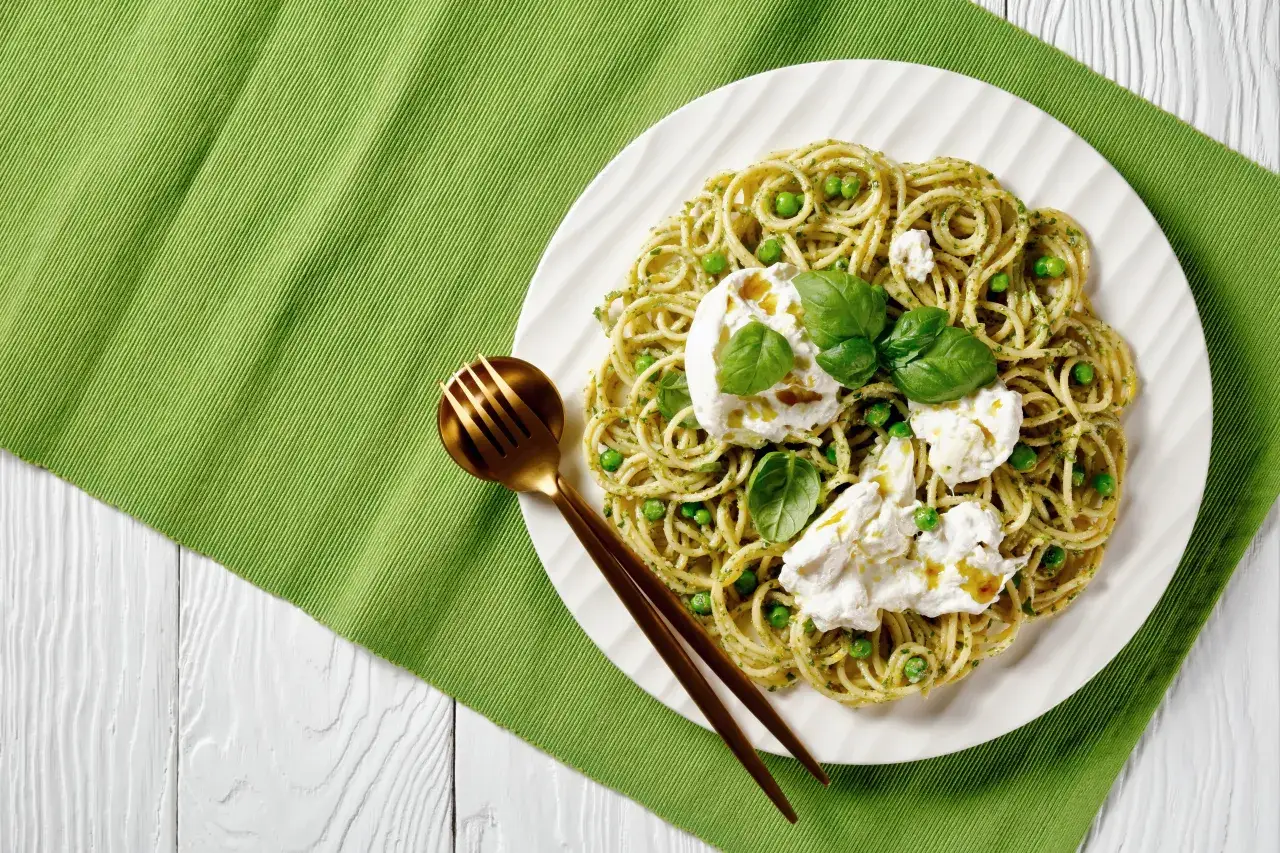 Pyszne włoskie dania z makaronem, jak spaghetti z groszkiem i burratą, na zielonym tle.
