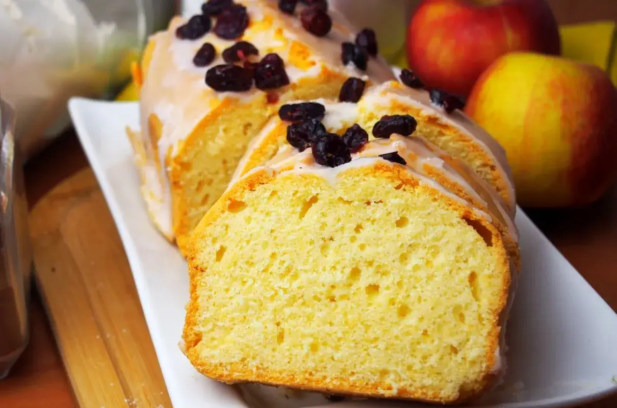 Szybka babka wilgotna, polana lukrem i posypana żurawiną, obok jabłek. Idealna na deser.