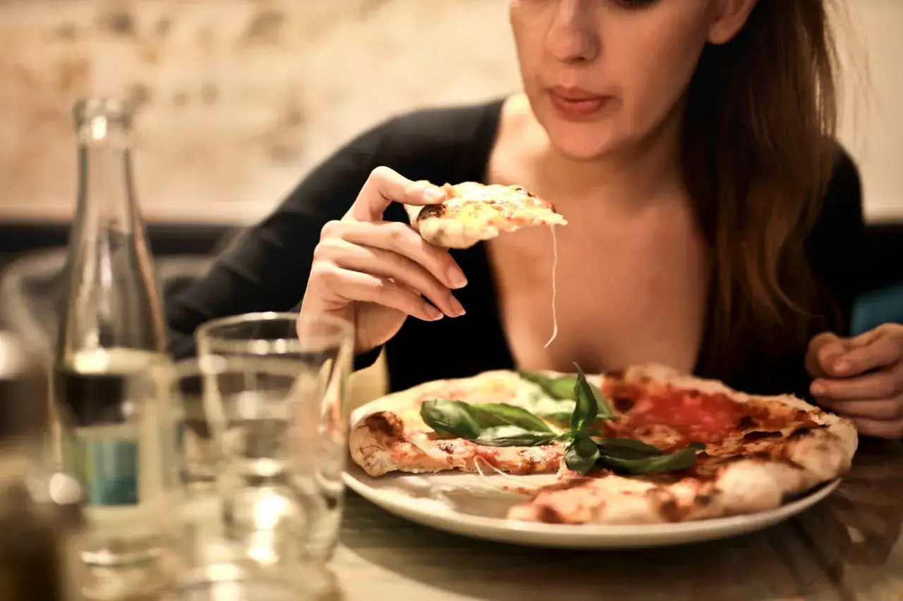 Smakowita pizza na talerzu, a ona bierze kawałek. Idealny wieczór we dwoje z pizzą.