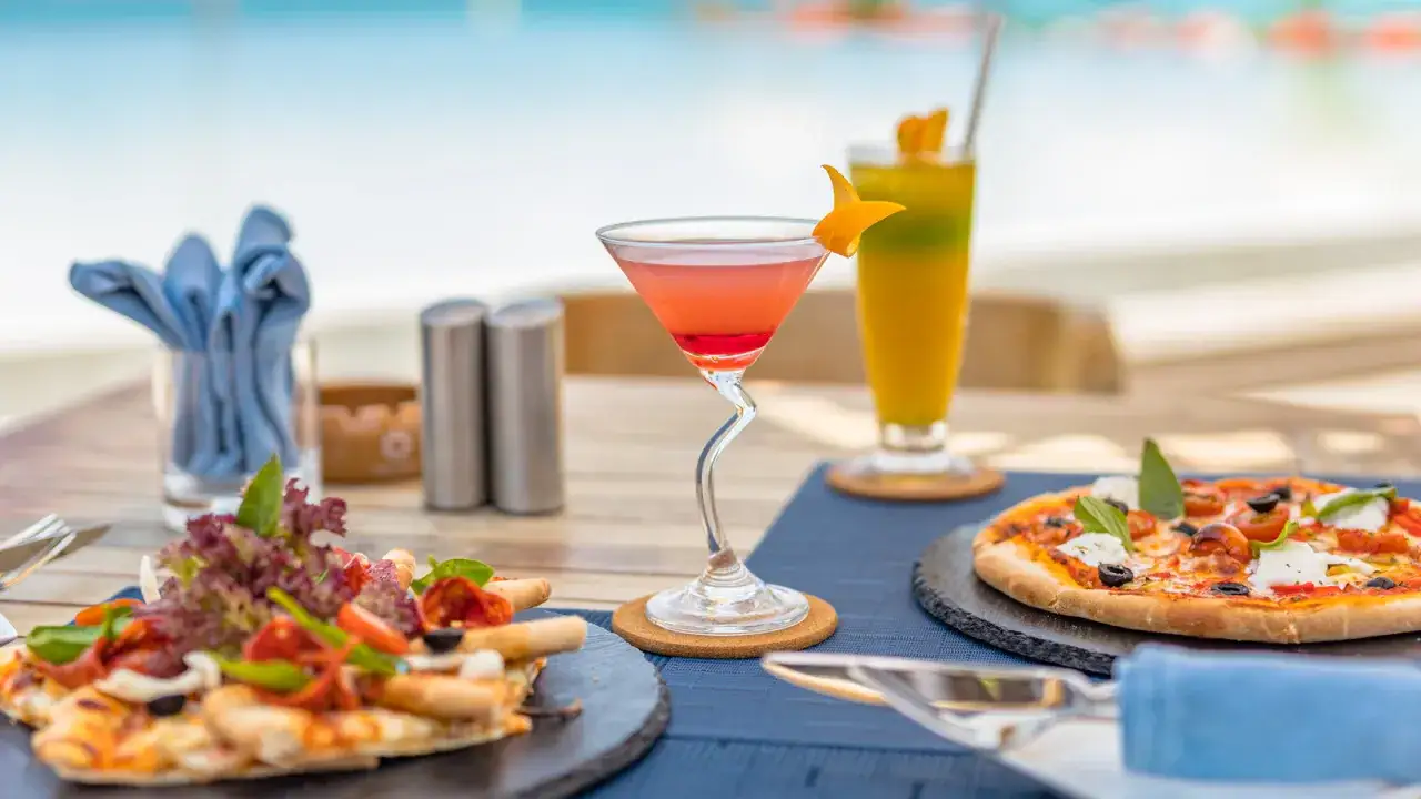 Dwa popularne drinki i pizze na stole przy basenie.