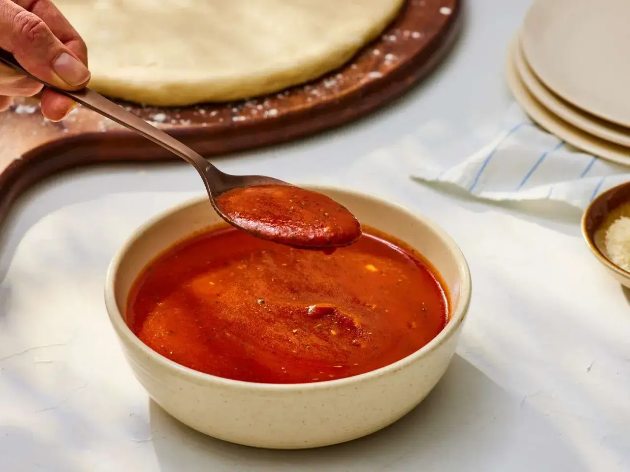 Łyżka nabiera aromatyczny sos pomidorowy z miseczki, gotowy do posmarowania ciasta na pizzę.